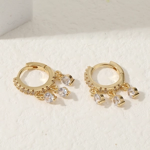 Elegantes pendientes huggie dorados con colgantes de circonita sobre fondo blanco