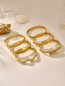 Close-up of six gold-plated bangles with zirconia inlay on a warm sandy background