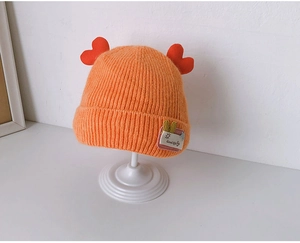 Detail of orange knitted baby hat with red heart pom-poms and Good Life text patch