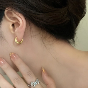 Close-up of minimalist gold hoop earrings and a silver bow ring with zircon stones