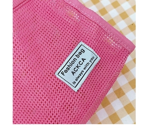 Detail of pink mesh travel wash bag featuring a honeycomb texture and a white woven label