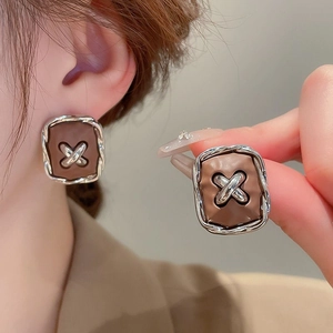 Close-up of square stud earring with silver braided edge and brown textured leather base