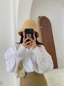 Close-up of a white long-sleeve blouse with puff sleeves paired with a yellow raffia hat