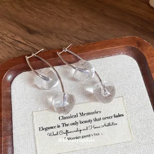 Elegant silver cherry drop earrings with clear glass pendants on a natural wooden tray