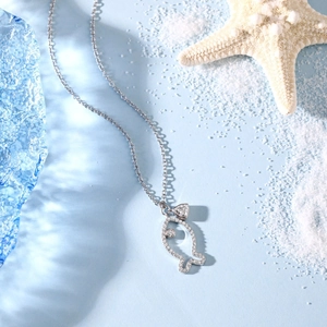 Detail of silver fish pendant with heart-shaped zircon on a beach-themed background