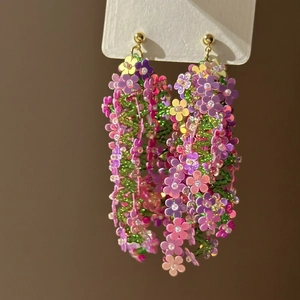Close-up of long tassel flower earrings with purple and yellow sequins and green beads