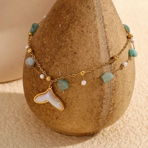 Close-up of 18K gold double-layered anklet with green stone and fish tail pendant