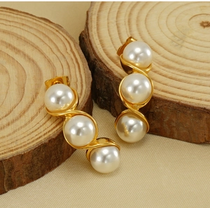 Detailed view of gold pearl pea earrings with three white pearls on a rustic wood background