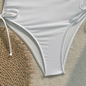 Gros plan du bas de bikini blanc avec cordons de serrage latéraux sur paille tissée