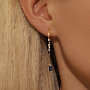 Detail of gold chain earrings with blue rectangular gemstone and white crystals