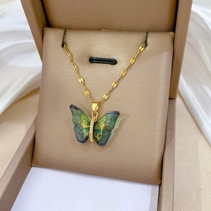 Macro shot of colorful butterfly pendant with blue-green wings and gold chain on velvet
