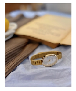 Detailed close-up of a vintage oval gold watch with a white dial on a soft fabric background