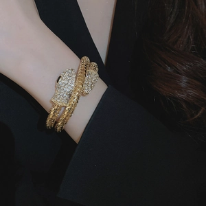 Detailed view of wrap-around gold snake bracelet with sparkling crystals on black blazer