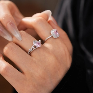 Close-up of two pink zircon crown rings on fingers featuring emerald and round cuts