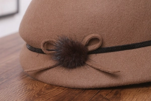 Détail d'un chapeau cloche en laine marron avec ruban à paillettes et pompon en fourrure