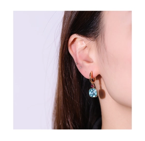 Detail of faceted rectangle blue gemstone and red crystal drop on gold hoop earring