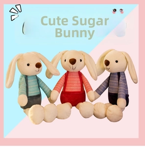 Detailed view of three plush rabbits wearing colorful striped overalls on a dual-tone background