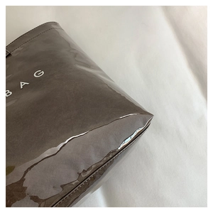 Close-up of glossy dark coffee leather tote bag featuring a white BAG text print