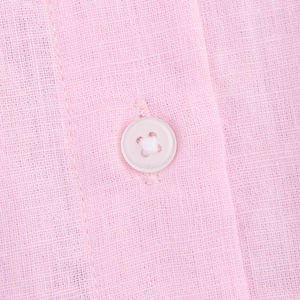 Close-up of a white four-hole button on pink linen fabric showing natural texture
