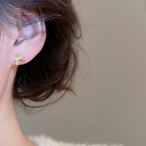 Détail d'une boucle d'oreille feuille de ginkgo dorée avec perle portée sur l'oreille