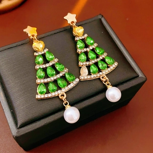 Macro shot of gold Christmas tree earrings with green gemstones and white pearl drops