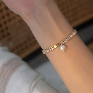 Détail d'un bracelet doré orné d'un zircon rectangulaire et d'une perle d'eau douce raffinée