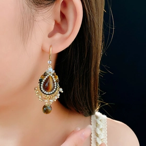 Close-up of vintage drop earring with tiger eye stone and zircon crystals on model