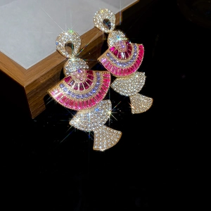 Detailed view of fan-shaped gold earrings with pink and purple rhinestones on a wooden box