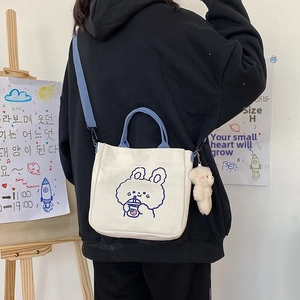 Detail of white canvas tote bag with blue rabbit print and cute bear plush pendant charm