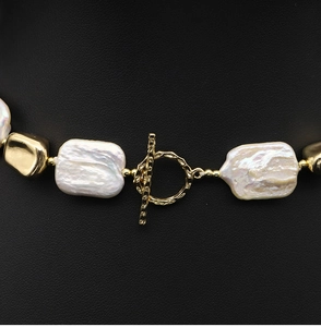 Macro detail of baroque pearls and golden OT clasp on a black leather background