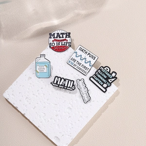 Flat lay of math themed enamel pins with formulas and text on a white textured pad