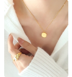 Detail of octagonal gold pendant necklace and sparkling zircon ring on a knit sweater