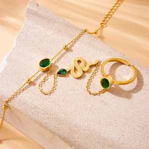 Gold snake ring bracelet set with green gemstones on minimalist stone background