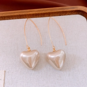 Gros plan détaillé de boucles d'oreilles crochet dorées avec pendentifs perle en cœur