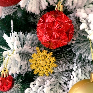 Macro shot of red polyhedral and gold snowflake ornaments on snowy Christmas tree branches