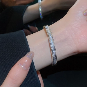 Close-up of a silver zircon paved luxury bracelet worn on a wrist with black suit sleeve