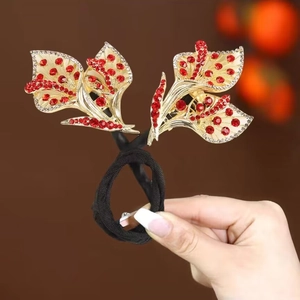 Détail d'un accessoire cheveux avec feuilles dorées, strass rouges et élastique noir