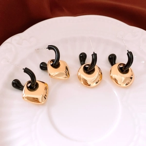Macro shot of geometric gold pendants with black C-hooks on white ceramic plate