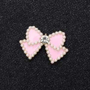 Pink bow jewelry charm with white pearls and central rhinestone on black background