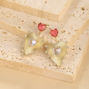 Detail of gold-plated heart earrings with red and clear zircon stones on a stone base