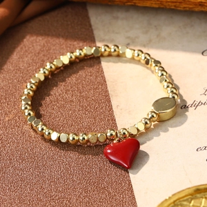 Close-up of golden beaded elastic bracelet with a red heart oil-drop pendant