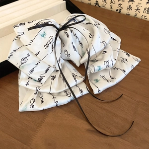 Detail of white satin bow hair claw with black ink calligraphy pattern and ribbons