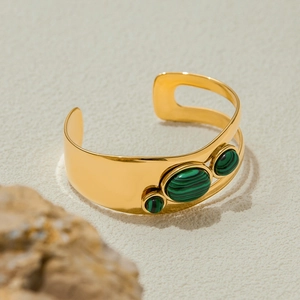Detail view of gold open cuff bracelet with three green malachite stones on beige stone