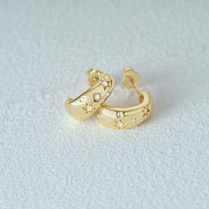 Detailed close-up of golden C-shaped hoop earrings with engraved stars and zircons
