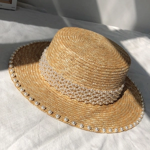 Close-up of woven straw hat with white faux pearl embellishments and natural fiber texture