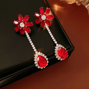 Close-up of elegant red zircon flower drop earrings on a premium black leather surface