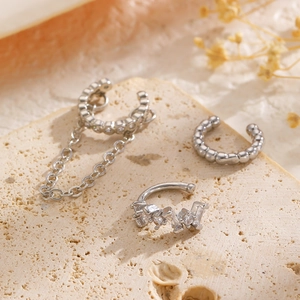 Primer plano de pendientes de clip plateados con cadenas y circonitas en piedra natural