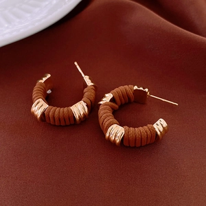 Detailed close-up of brown textured leather wrap hoop earrings on red velvet surface