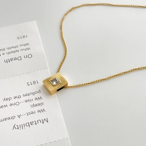 Close-up of golden titanium necklace with square sunburst pendant and clear zircon stone