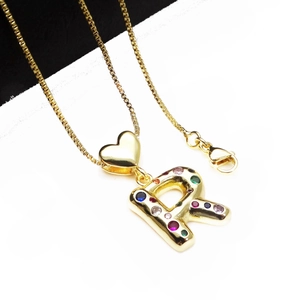Detailed shot of gold letter R pendant with colorful zircons and small heart charm